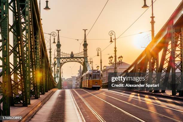 historic yellow tram moving on liberty bridge at sunrise, budapest, hungary - budapest skyline stock pictures, royalty-free photos & images