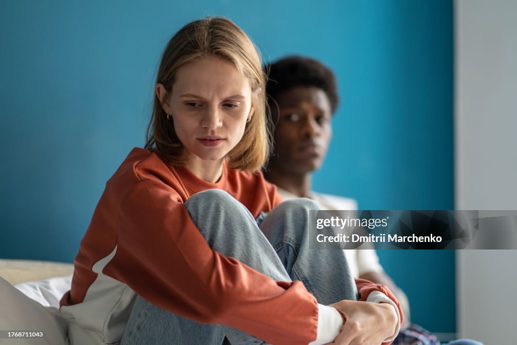 Upset confused frustrated multi ethnic girl guy sitting in bed after quarrel offended each other.