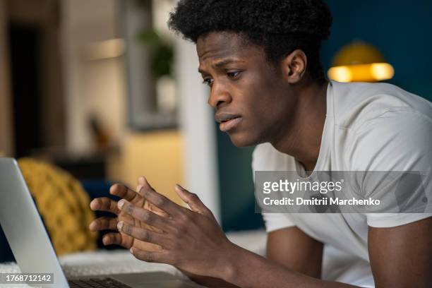 sad frustrated african american guy gamer plays on laptop lost the video game lying in bed at home. - georgian man stock pictures, royalty-free photos & images