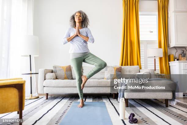 senior woman doing yoga in living room - tree position stock pictures, royalty-free photos & images