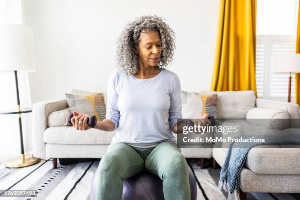 senior woman lifting weights in living room - poids-et-haltères photos et images de collection