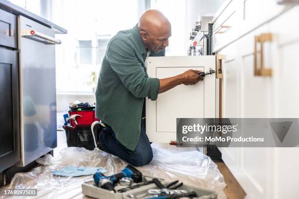 senior man repairing kitchen cabinet at home - home improvement stock pictures, royalty-free photos & images