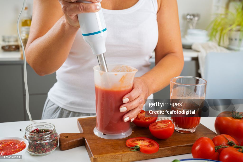 Woman using immersion blender to prepare tomato juice in the morning for a healthy breakfast