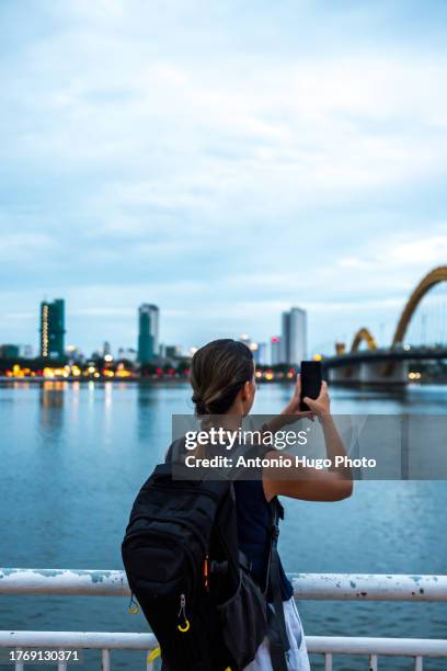 young woman taking a photo of da nang city and dragon bridge in vietnam at sunset. digital nomad concept - river han stock pictures, royalty-free photos & images