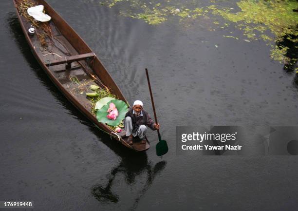 An elderly man rows a boat carrying a bouquet of lotus flowers on Da lake August 19, 2013 in Srinagar, the summer capital of Indian administered...