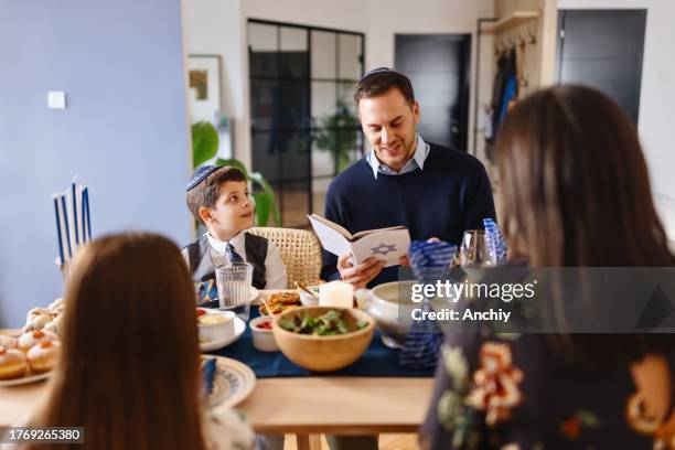 père souriant lisant la bible hébraïque pendant le dîner traditionnel de hanoukka à la table à manger - juif photos et images de collection