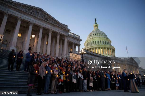 At right, U.S Speaker of the House Mike Johnson bows his head while delivering a prayer during a bipartisan candlelight vigil with members of...