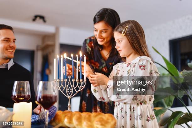 little girl lighting menorah with her mother - igniting stock pictures, royalty-free photos & images