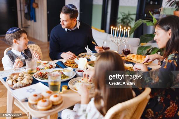 smiling family eating traditional jewish food on hanukkah - sufganiyah stock pictures, royalty-free photos & images