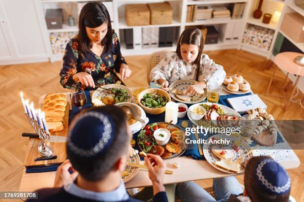 jewish family eating at the dining table during traditional hanukkah dinner - sufganiyah stock pictures, royalty-free photos & images