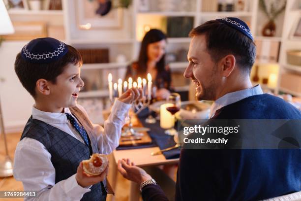 close-up of a smiling son and his father eating sufganiyot on hanukkah - sufganiyah stock pictures, royalty-free photos & images