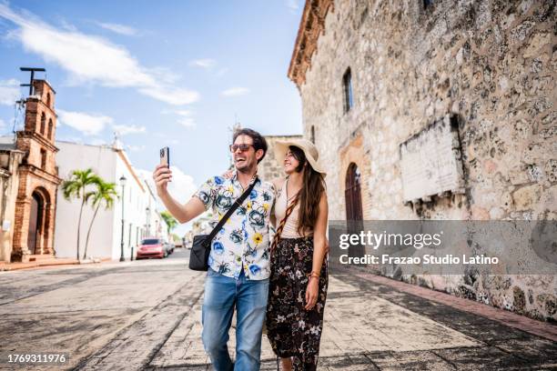 couple de touristes prenant un selfie ou filmant à l’aide d’un téléphone portable dans un quartier historique - saint domingue république dominicaine photos et images de collection