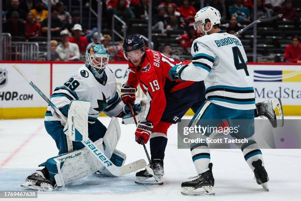 Nicklas Backstrom of the Washington Capitals fights for position against Mackenzie Blackwood and Kyle Burroughs of the San Jose Sharks during the...