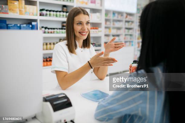 ドラッグストアのレジカウンターでお客さんをお手伝いするフレンドリーな女性薬剤師 - 女性薬剤師 ストックフォトと画像