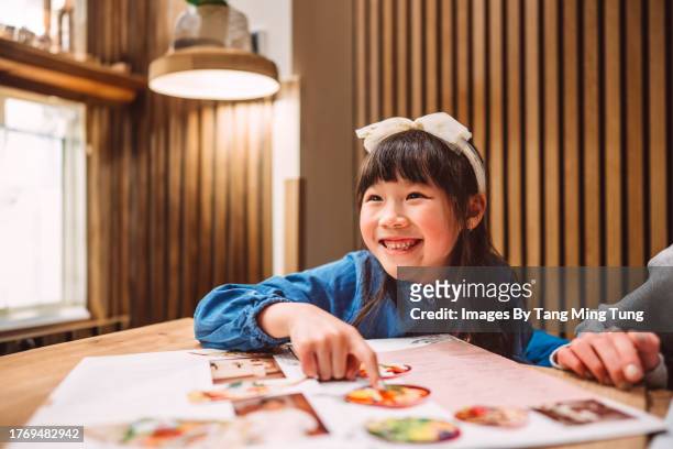 lovely cheerful girl looking at food menu while dining out with family in a japanese restaurant - kids menu photos et images de collection