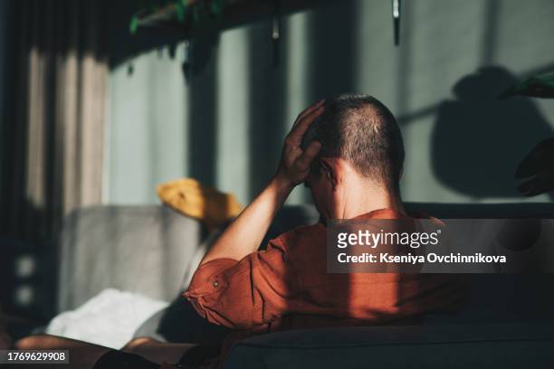 unpleasant pain. sad unhappy handsome man sitting on the sofa and holding his forehead while having headache - suicide fotografías e imágenes de stock