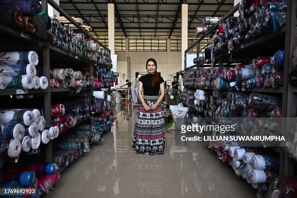 This photo taken on October 18, 2023 shows factory owner and director Kingkarn Samon standing in between shelves holding bolts of elephant print...