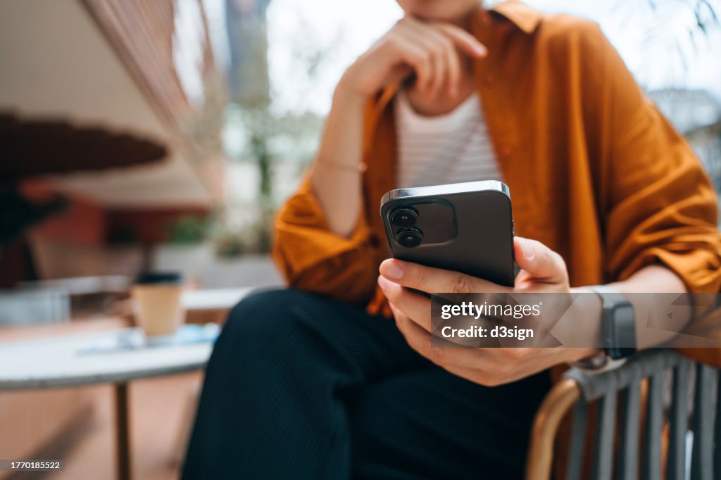 Close up shot of a young Asian woman using smartphone while sitting in an outdoor cafe and drinking coffee. Lifestyle and technology