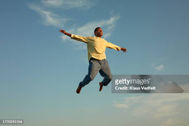 man with arms outstretched jumping against sky - mann freudensprung sonne vorderansicht leger stock-fotos und bilder