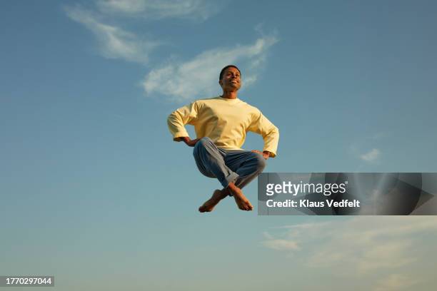 man levitating with cross-legged against sky - gambe incrociate foto e immagini stock