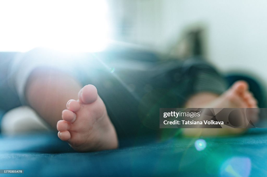 Overexposed photo of small feet of infant child lying on blue coach under sunlight
