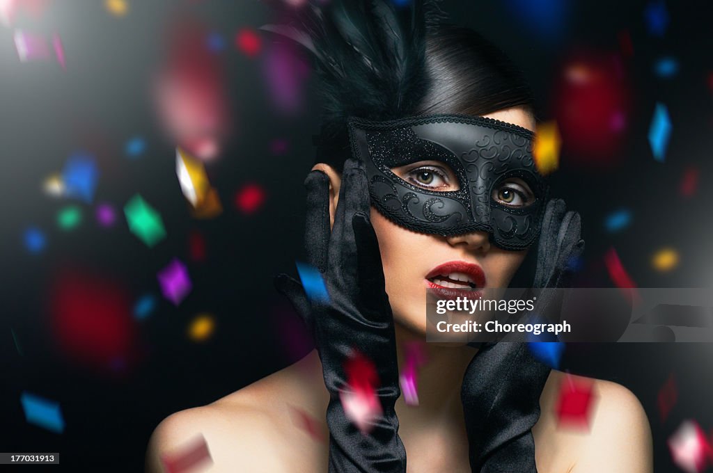 Female wearing a black masquerade mask with confetti falling