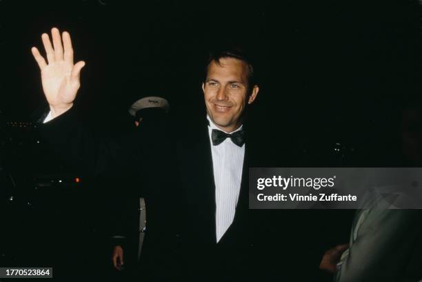 Kevin Costner wearing a tuxedo, waves at fans after arriving at the AFI Awards, United States, circa 1990s.