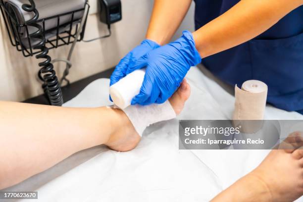 nurse putting foot bandages on a leg wound on a patient sitting on the stretcher. health center or emergency hospital - leg wound stockfoto's en -beelden