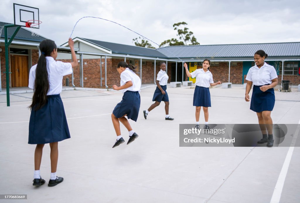 School children playing jump rope game in school yard during recess