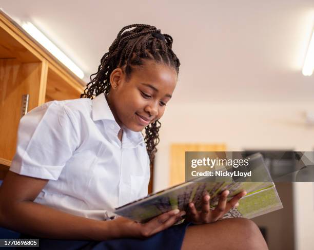 happy schoolgirl reading a book sitting at school library - cute college girl stock pictures, royalty-free photos & images
