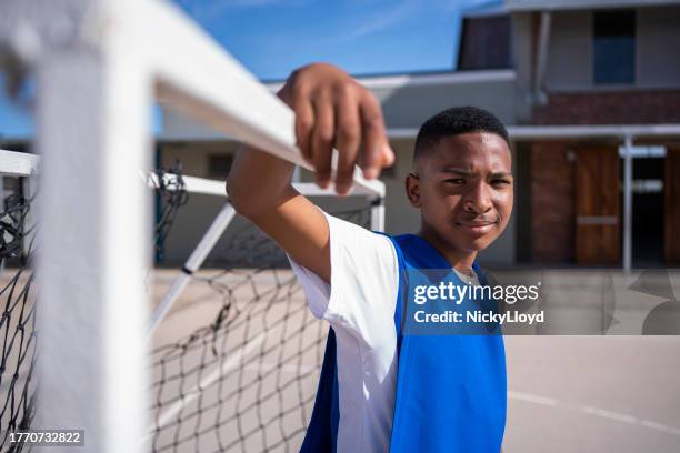 schoolboy soccer player standing at goal post in playground - boy goalie standing in front of goal net stock pictures, royalty-free photos & images