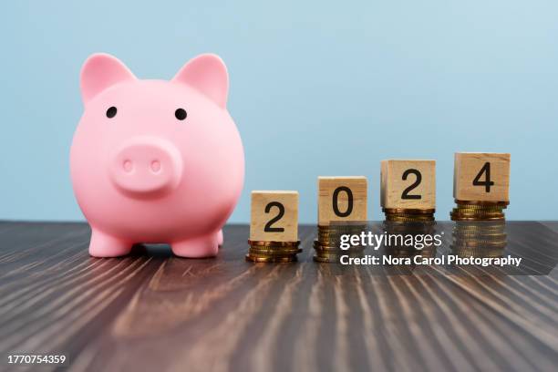 new year 2024 on wood block on top of stack of gold coins and piggy bank - carol grow stock-fotos und bilder