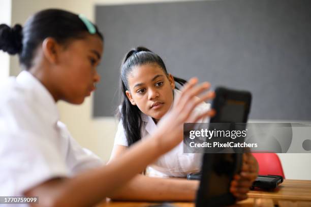 schoolgirl helping classmate on digital tablet in class - educational subject stock pictures, royalty-free photos & images