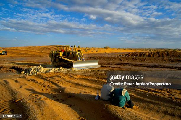 Workers watch a bulldozer backfilling a trench containing sealed and completed pipe sections during construction of the Maghreb-Europe Gas Pipeline...