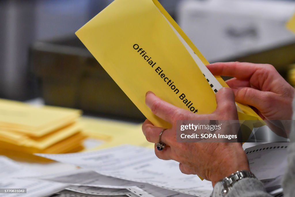 A woman takes a mail-in ballot from an envelope at a polling...