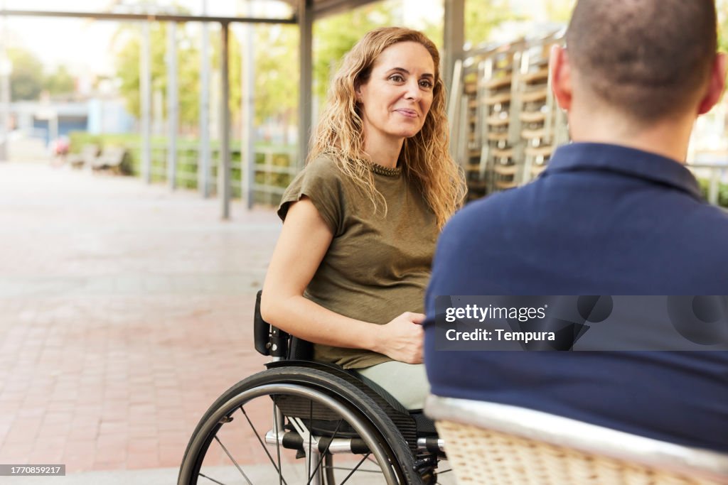 Inklusive Café: Eine Frau, schwanger und im Rollstuhl, sitzt auf der Terrasse und beobachtet ihre Freundin aus dem Bild.