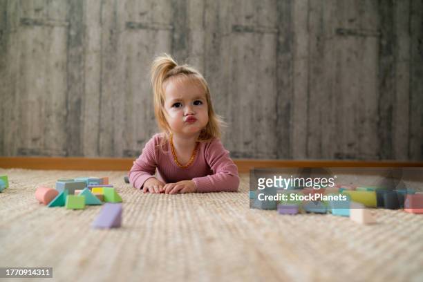 cute girl making a face while lying on the carpet at home - baby blocks stock pictures, royalty-free photos & images