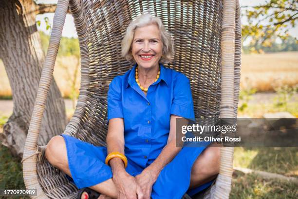 portrait of smiling senior womansitting in hanging chair - blue blouse stock pictures, royalty-free photos & images