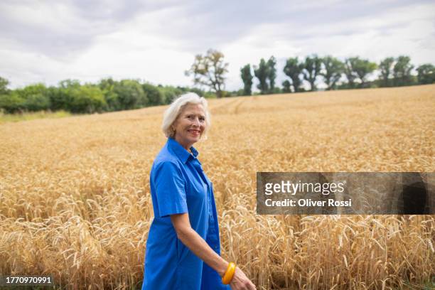 smiling senior woman walking at grain field - blue blouse stock pictures, royalty-free photos & images