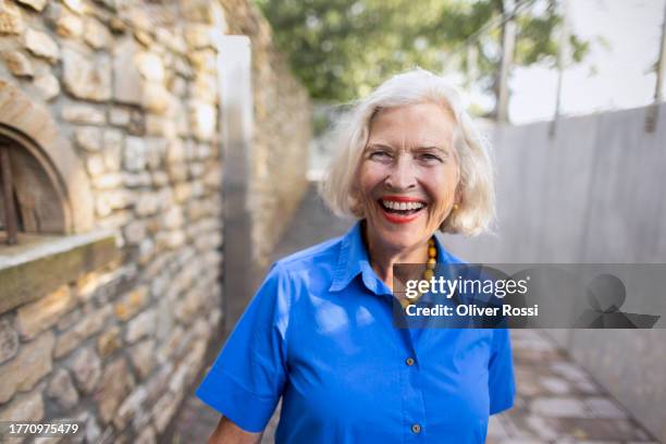 portrait of laughing senior woman on footpath at stone wall - blue blouse - fotografias e filmes do acervo