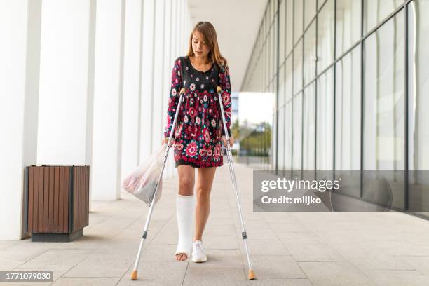woman with crutches walking down the outside corridor - trash bag dress stock pictures, royalty-free photos & images
