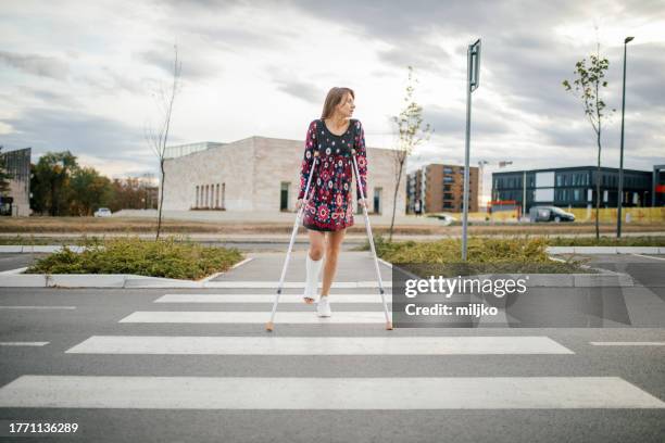 frau mit krücken überquert die straße - gehgips stock-fotos und bilder
