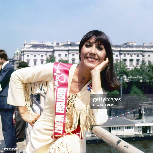 Portrait of British singer and actress Anita Harris, with a sash that reads 'British Heart Foundation,' as she stands on Waterloo Bridge, London,...