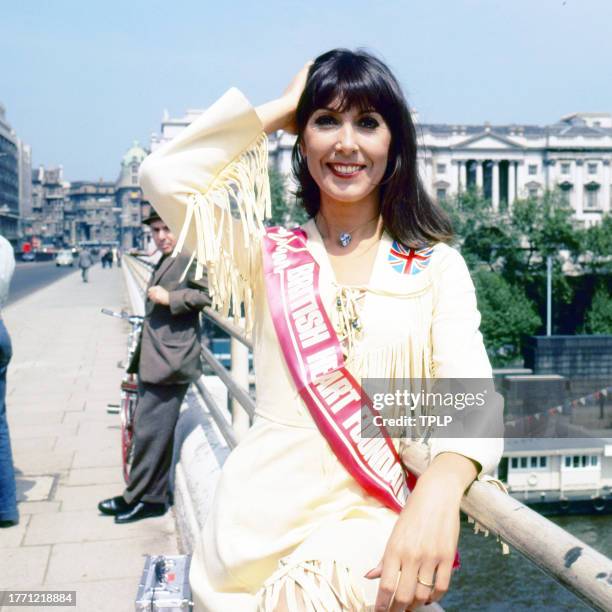 Portrait of British singer and actress Anita Harris, with a sash that reads 'British Heart Foundation,' as she stands on Waterloo Bridge, London,...