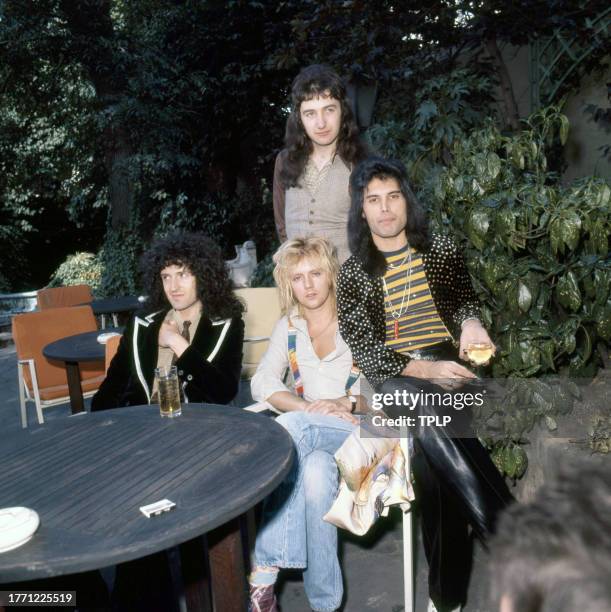 View of members of the Rock and Pop group Queen as they pose at an outdoor table, London, England, September 8, 1976. Pictured are, seated from left,...