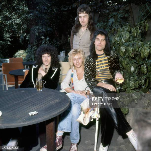 View of members of the Rock and Pop group Queen as they pose at an outdoor table, London, England, September 8, 1976. Pictured are, seated from left,...
