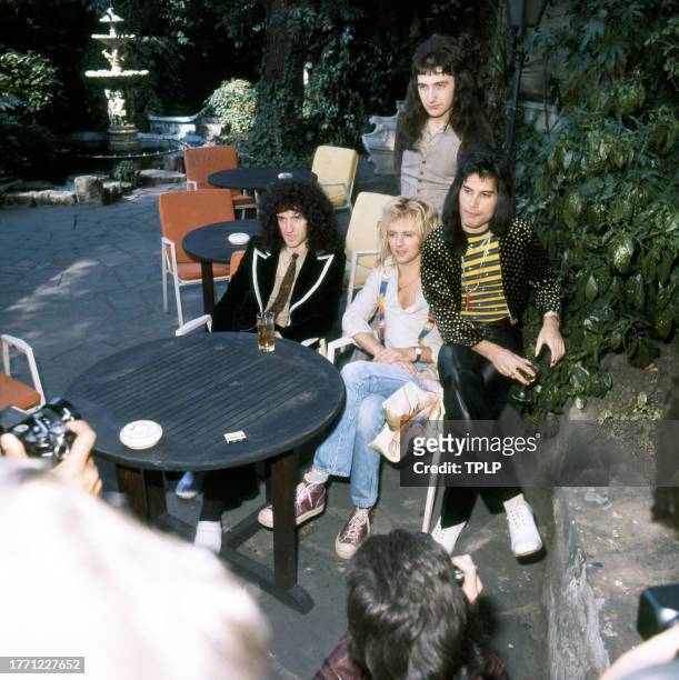 View of members of the Rock and Pop group Queen as they pose at an outdoor table, London, England, September 8, 1976. Pictured are, seated from left,...