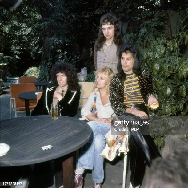 View of members of the Rock and Pop group Queen as they pose at an outdoor table, London, England, September 8, 1976. Pictured are, seated from left,...