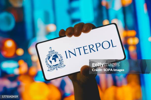 In this photo illustration, the International Criminal Police Organization logo is displayed on a smartphone screen.