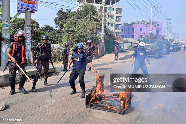 Bangladeshi security personnel personnel work to remove burning items placed along a road by garment workers protesting in Gazipur on November 9...